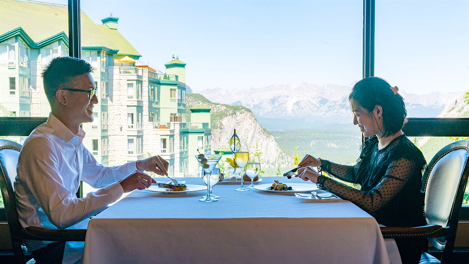 Two people dining at Eden, with views of mountains in the background; on the table are a glass of wine and a Martini